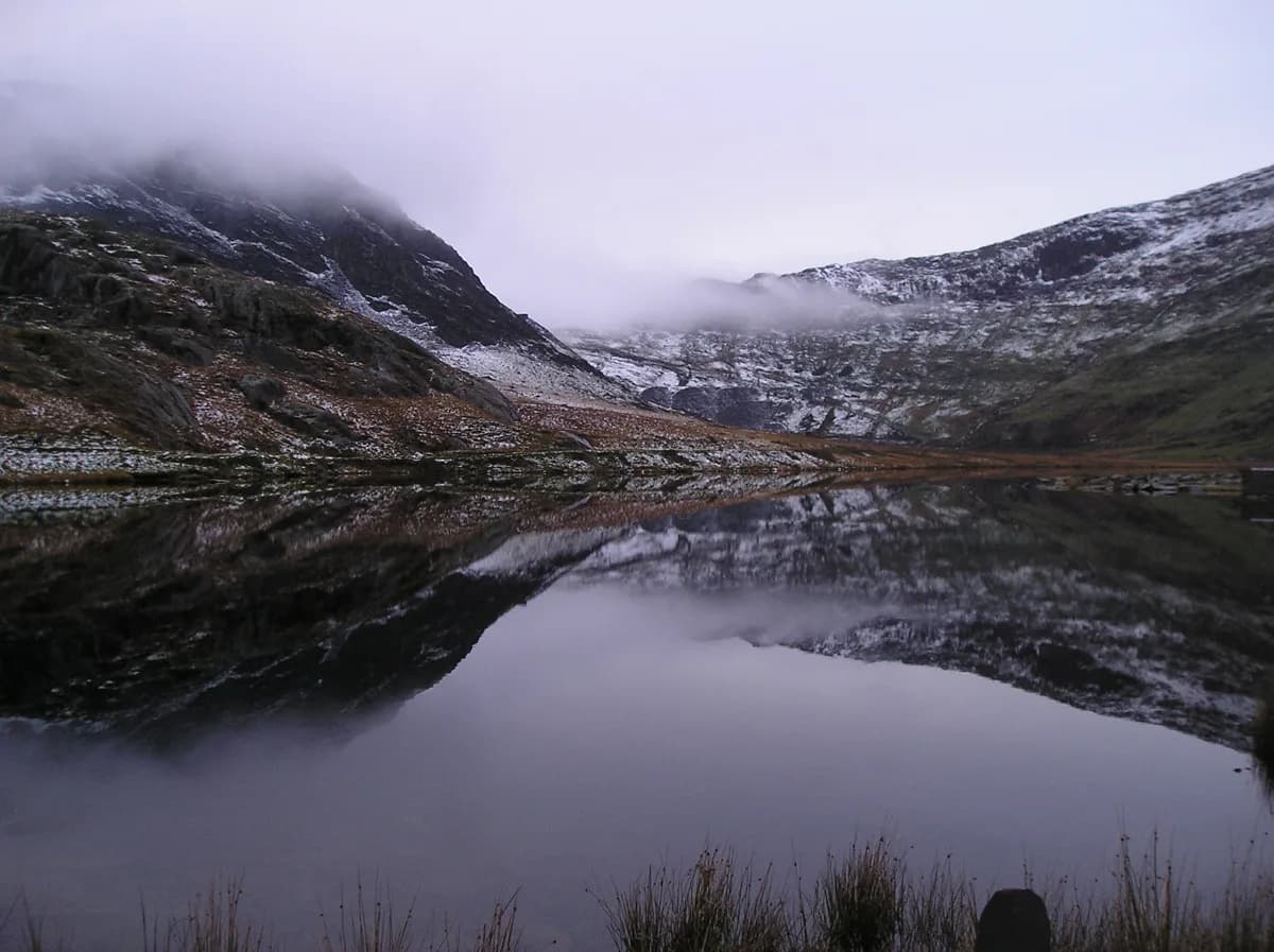 Misty mountain lake (Llyn Cwmorthin) reflecting snow-capped cliffs in Snowdonia, north Wales.
