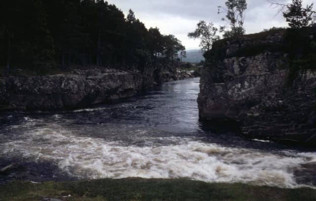 A fast-flowing river churning through a rocky gorge lined with trees near Garve, Scotland.