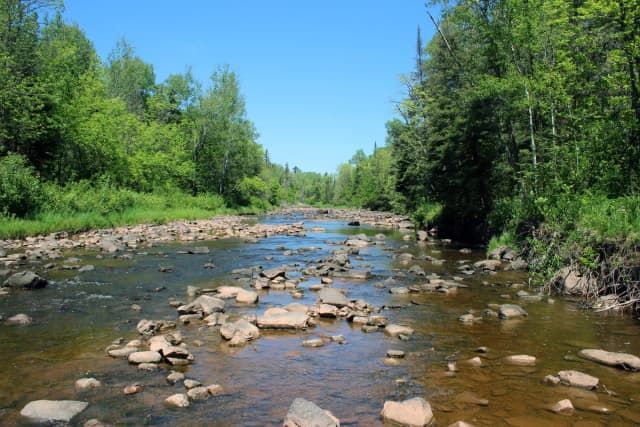 Wide view of the rocky Knife River flowing through forest on the North Shore of Minnesota on a sunny day