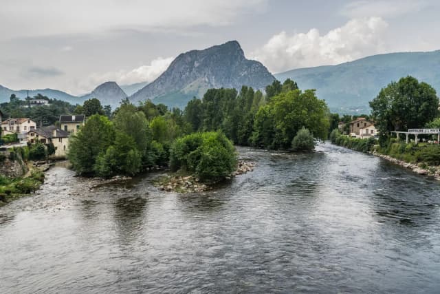 The Ariège River flowing through the town of Tarascon-sur-Ariège in the French Pyrenees, with a rocky peak rising behind the rooftops.
