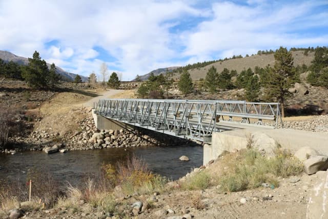 A metal truss bridge spanning the Arkansas River near Granite, Colorado, with mountains and pine trees in the background.