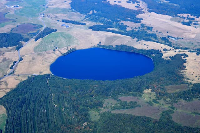 Aerial view of the round volcanic Lac Chauvet surrounded by forest and farmland in the Monts Dore, Puy-de-Dôme, France