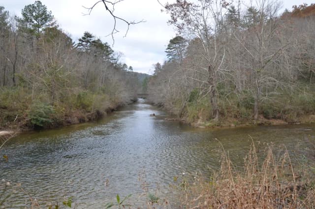 The Chattooga River flowing calmly between wooded banks, with a bridge visible in the distance.