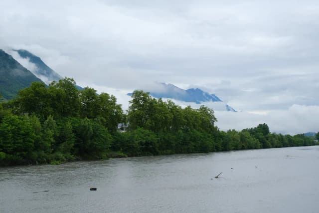 A wide alpine river flowing past tree-lined banks, with misty mountains in the background near Montmelian, Savoie.