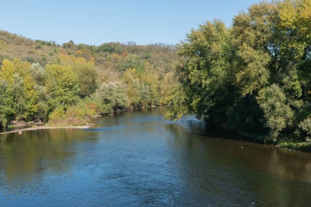 A wide, tree-lined stretch of the River Allier flowing calmly past wooded hillsides in autumn near Coudes, Puy-de-Dôme, France.