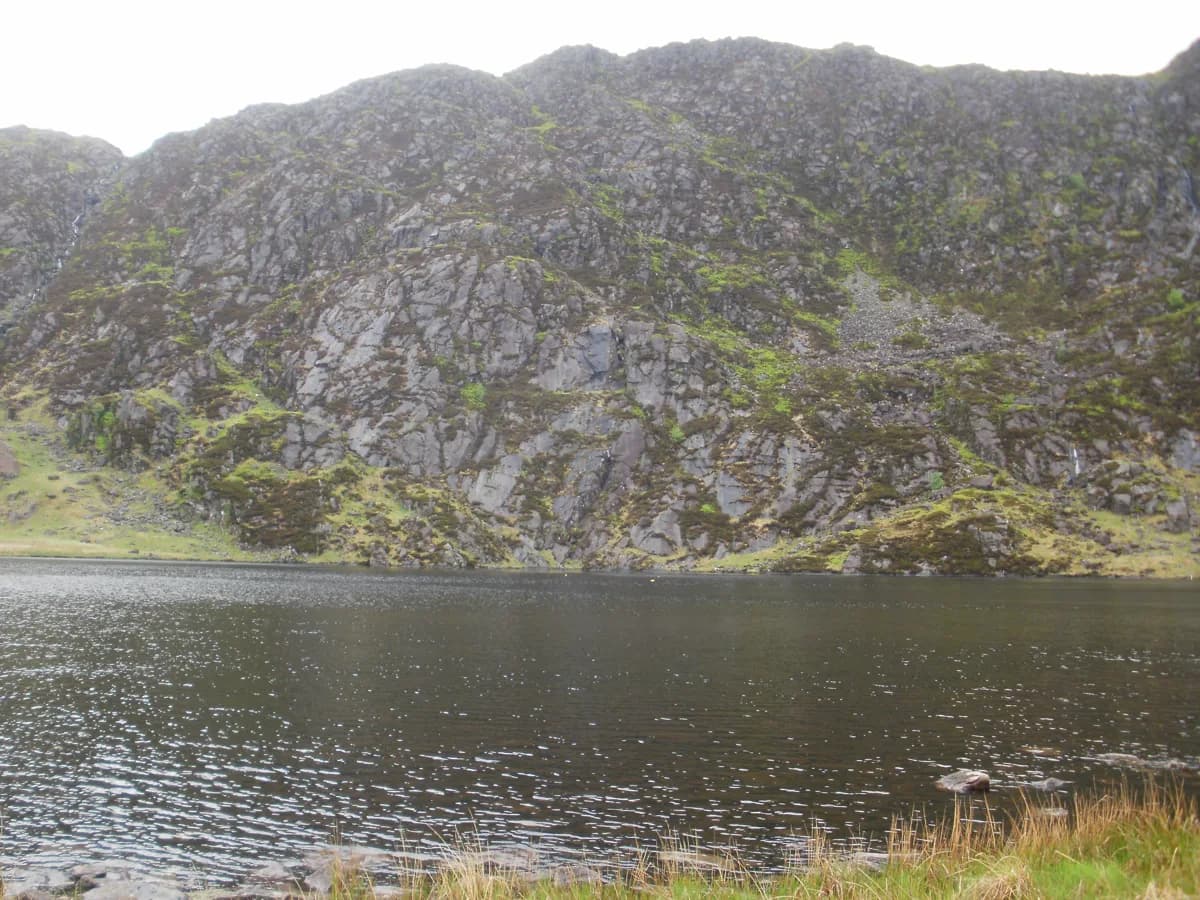 Dark mountain lake (Llyn Llagi) in Snowdonia backed by a steep rocky crag.