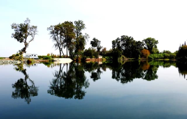 Still water on the Mokelumne River near Lodi, California, with trees and a small boat reflected on the surface.