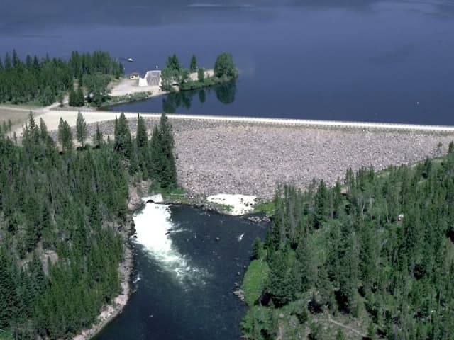 Aerial view of Island Park Dam holding back Island Park Reservoir, with the Henrys Fork River flowing out below the spillway