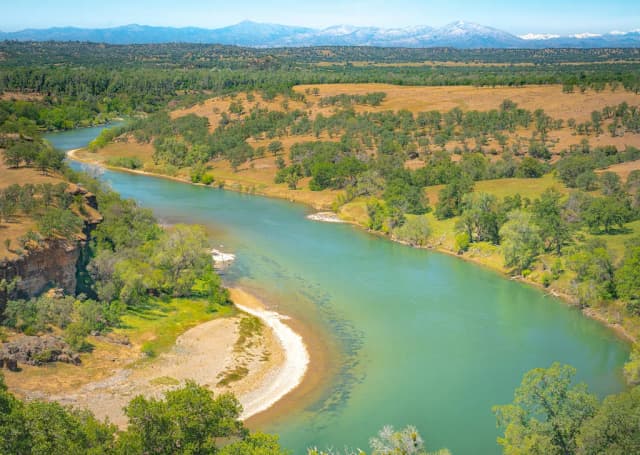 Aerial view of the turquoise Sacramento River bending through oak grassland with mountains in the distance.
