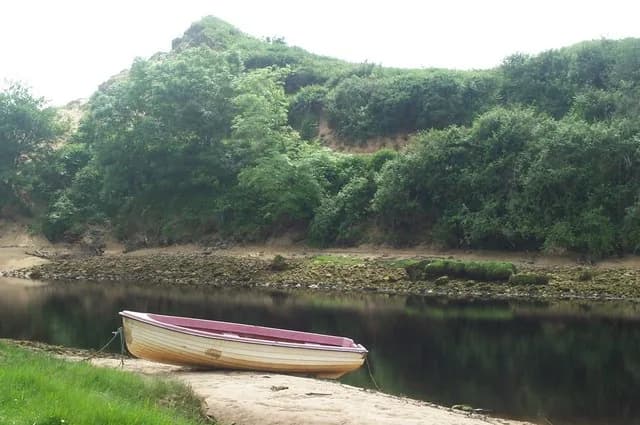 Eany Water meandering past wooded banks near Inver Bay, County Donegal, with a moored rowboat on the shore