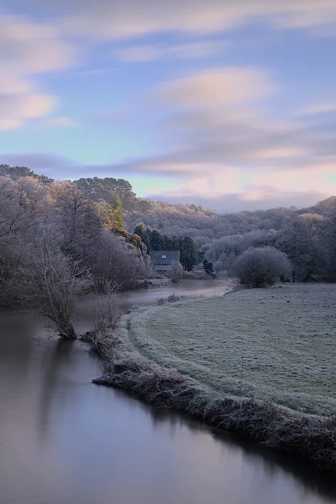 A frost-covered bend of the Léguer river at dawn, with a stone house among bare trees on the bank.