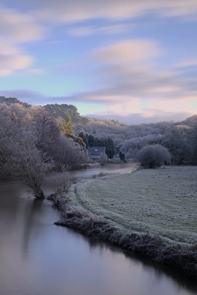 A frost-covered bend of the Léguer river at dawn, with a stone house among bare trees on the bank.