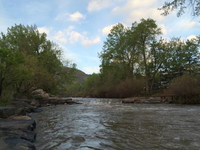 Clear Creek flowing over a small rapid lined with boulders in Golden, Colorado, foothills visible in the background.