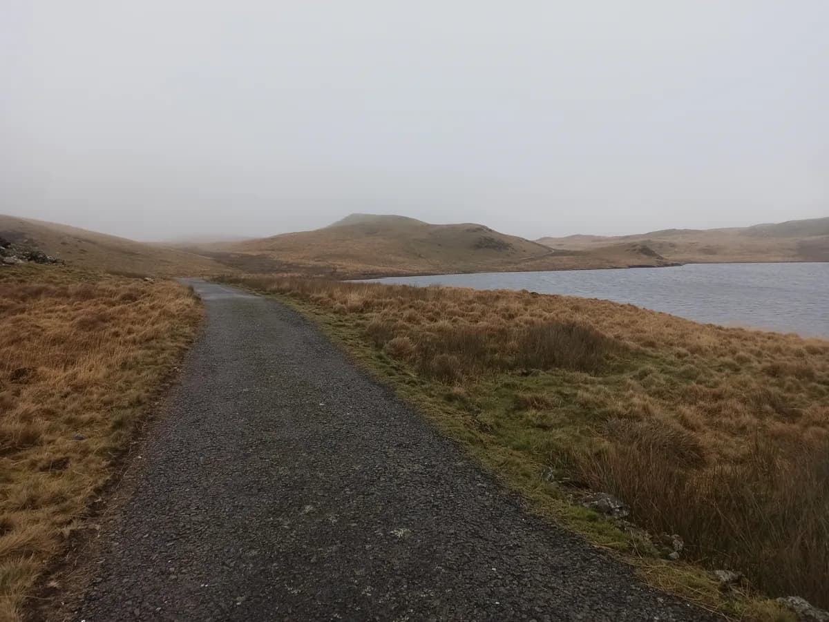 A gravel track beside Llyn Egnant, an upland lake in the Cambrian Mountains, Wales, with misty hills in the background.