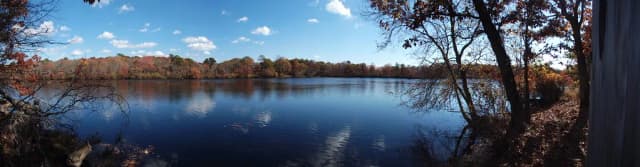A wide, still pond-like stretch of the Connetquot River surrounded by autumn trees, seen from a duck blind.