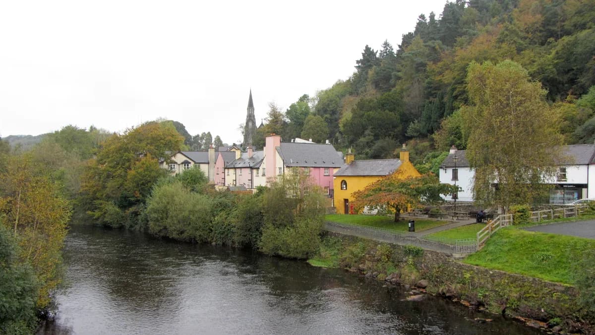 The Avoca River bending past colourful houses and a church spire in Avoca village, Co. Wicklow
