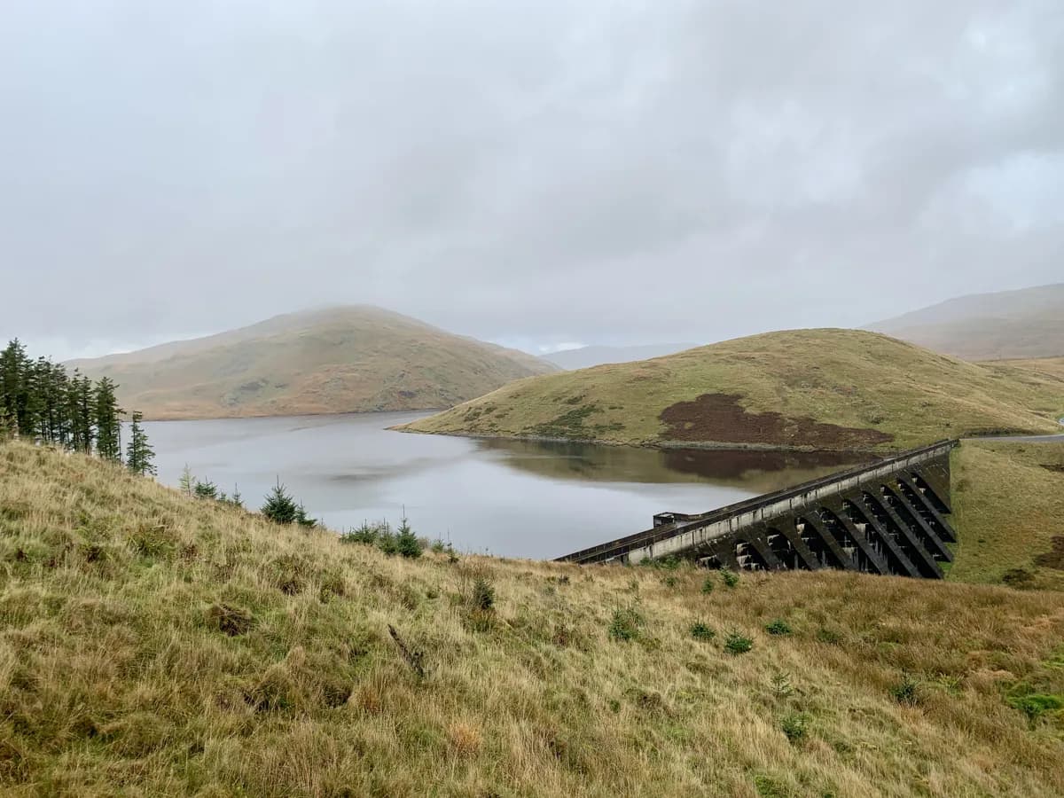 Misty view over Nant y Moch Reservoir in mid Wales, with the concrete dam structure on the right and rolling Cambrian Mountains hills surrounding the water.