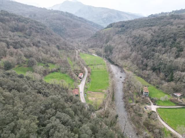 An aerial view of the Asón river winding through a green wooded valley with farmhouses and mountains in the background, in Ruesga, Cantabria, Spain.