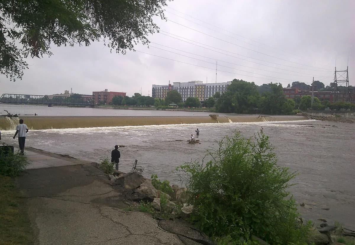 Wide view of the Grand River flowing over a low dam in downtown Grand Rapids, Michigan, with anglers wading in the current