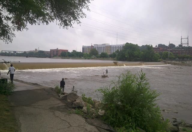 Wide view of the Grand River flowing over a low dam in downtown Grand Rapids, Michigan, with anglers wading in the current