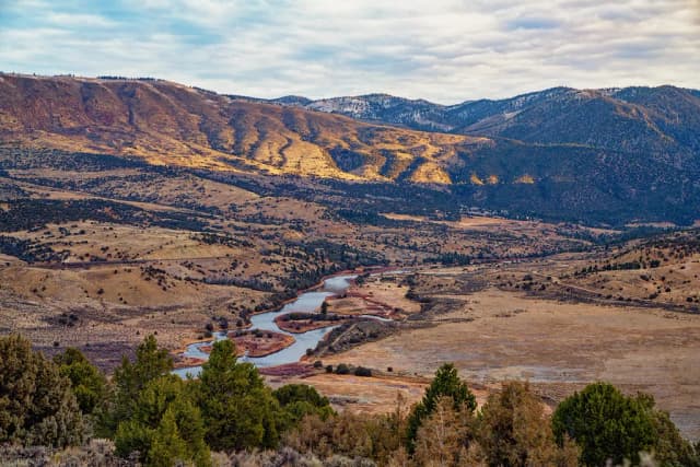 A wide valley view of the Colorado River meandering below golden autumn hillsides near Kremmling, Colorado.