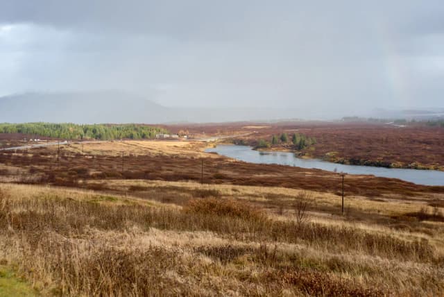 A wide river bending through open moorland with a distant road bridge and mountains, autumn colours in the vegetation, Sog river Iceland.