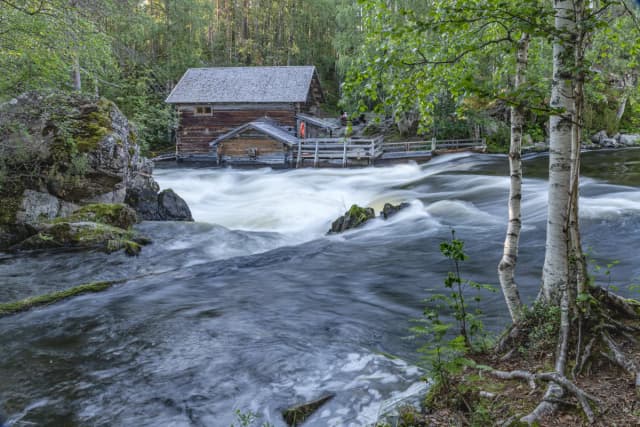 Wide view of whitewater rapids on the Kitkajoki River rushing past a historic wooden mill building in Kuusamo, Finland