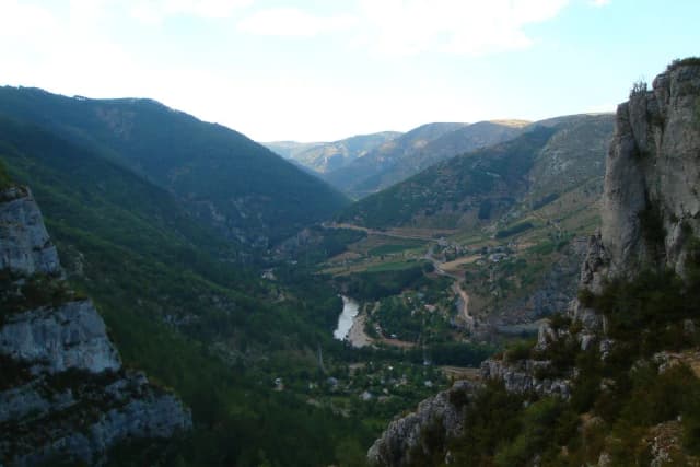 Aerial view of the Tarn river winding through the deep limestone Gorges du Tarn, with a village and wooded slopes visible.