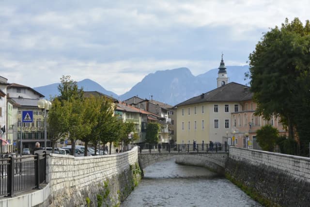 The Brenta river running through the historic centre of Borgo Valsugana with Alpine peaks and a bell tower in the background