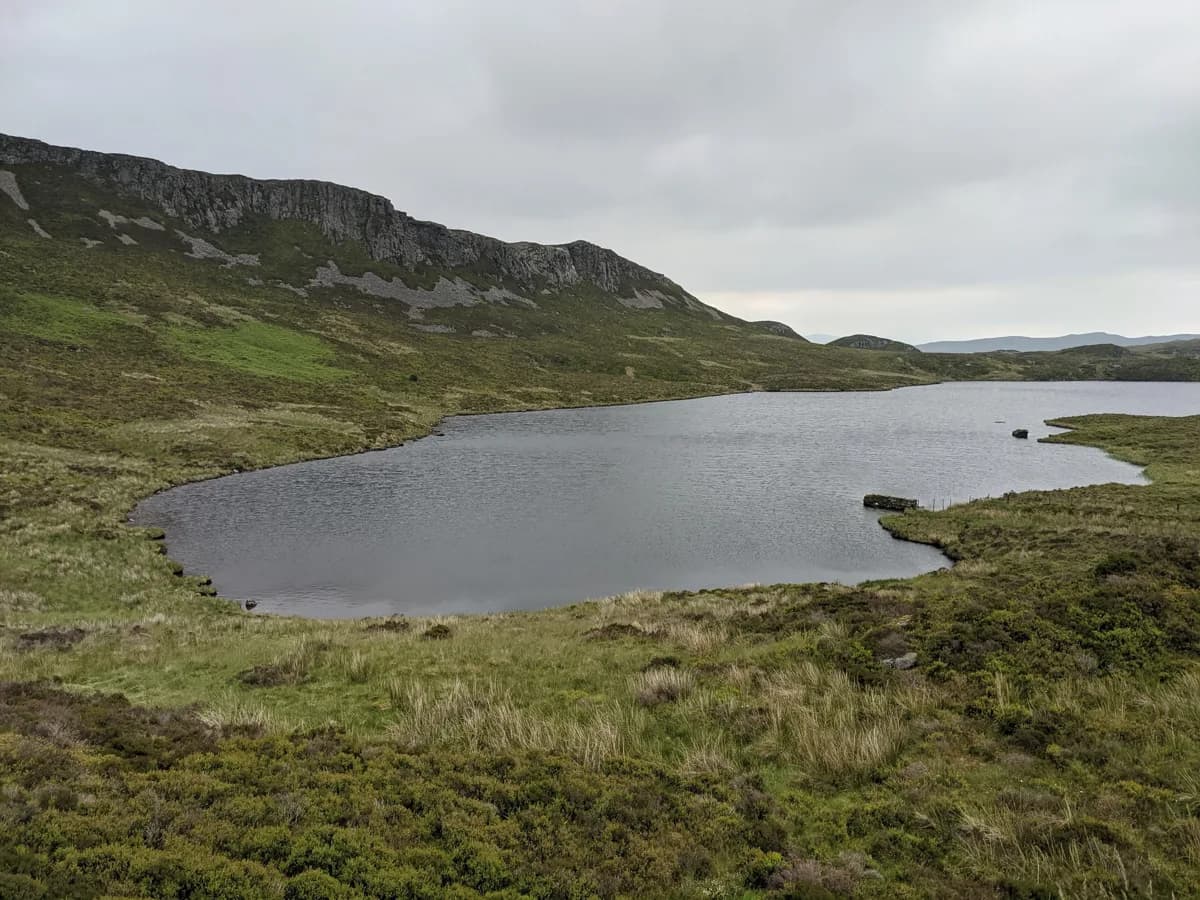 Upland lake (Llyn Gamallt Fawr) in Snowdonia with a rocky crag rising behind the far shore.