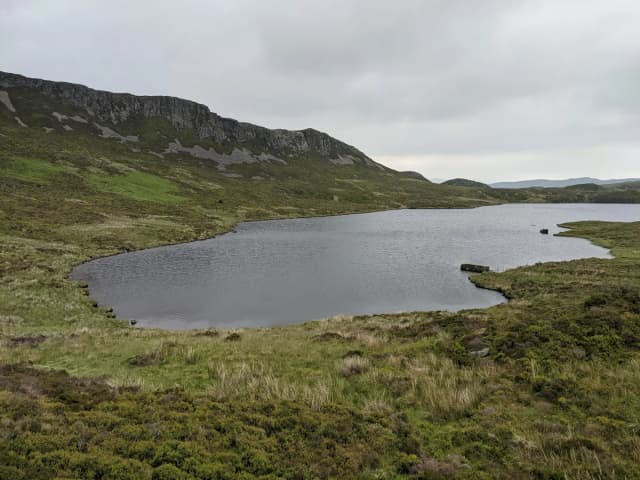 Upland lake (Llyn Gamallt Fawr) in Snowdonia with a rocky crag rising behind the far shore.