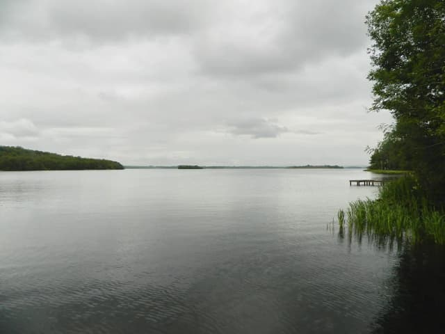 Calm, wide expanse of Lower Lough Erne under a cloudy sky, with wooded shoreline and a small jetty.