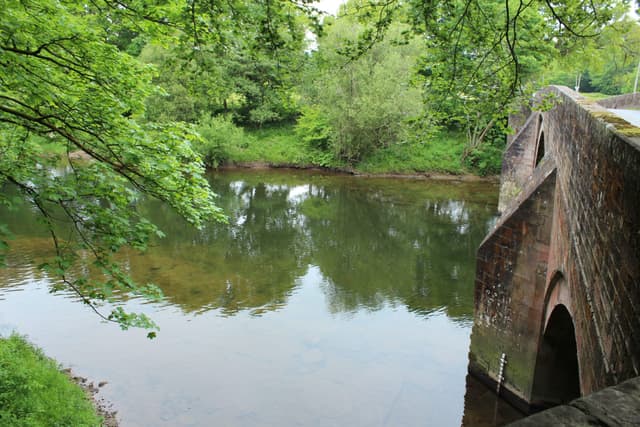 The River Annan at Hoddom Bridge, fast clear summer water over gravel with wooded banks.