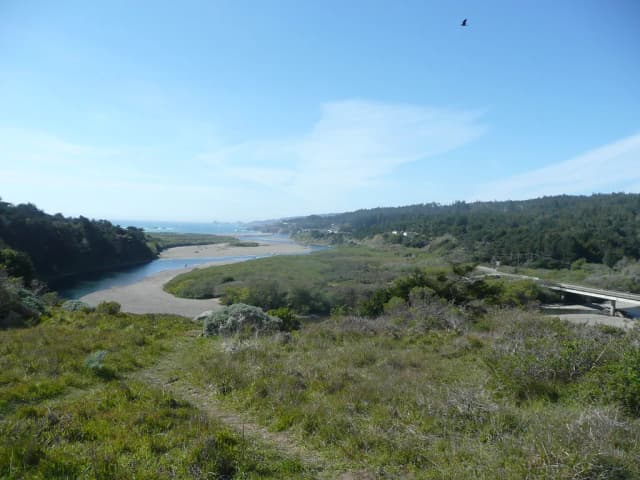 Aerial view of the Gualala River meandering through green coastal hills to meet the ocean.