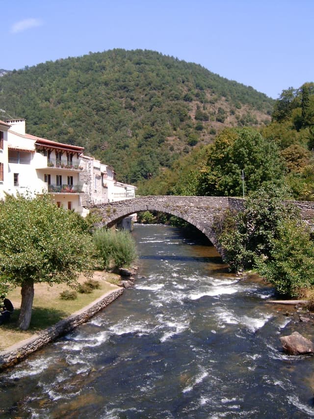 The Aude river flowing beneath a stone bridge at Axat, with wooded mountains behind