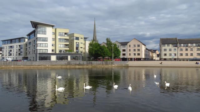 The River Barrow flowing through Carlow town, with swans on the water and St Mary's Church spire visible above the quayside buildings