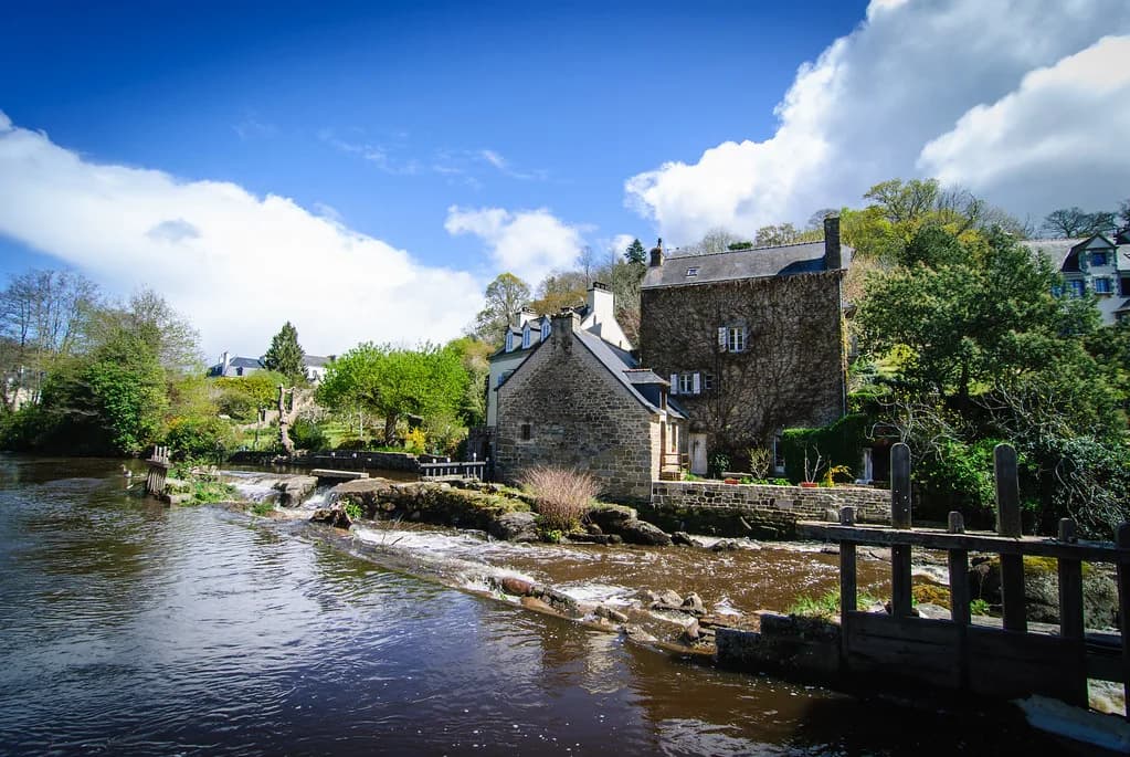 The River Aven flowing over a low weir past stone houses in Pont-Aven, Brittany, France.