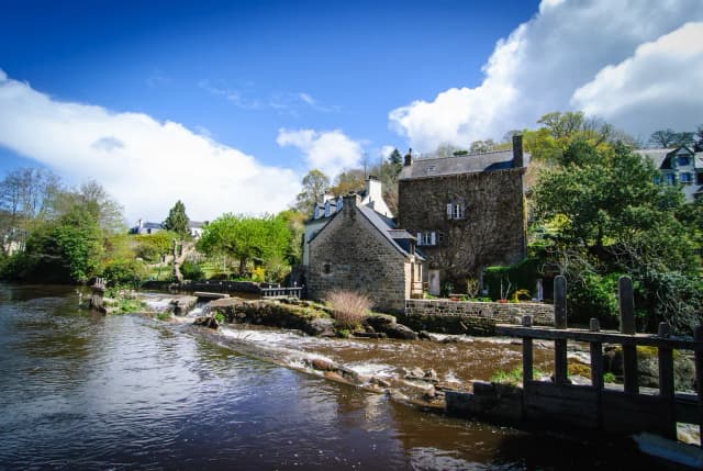 The River Aven flowing over a low weir past stone houses in Pont-Aven, Brittany, France.