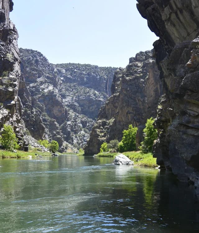 A narrow river flowing between towering dark canyon walls in the Gunnison Gorge, Colorado.
