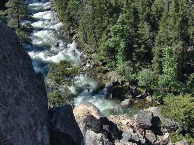 Fast whitewater cascading through a boulder-strewn canyon on the upper Boulder River in Sweet Grass County, Montana, flanked by conifer forest