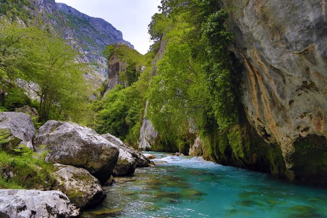 A deep turquoise pool on the Río Cares flanked by towering limestone walls below Puente de la Jaya.