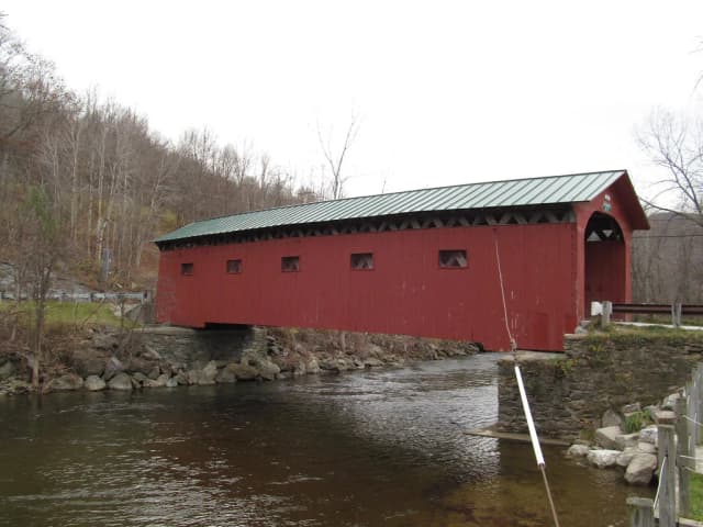 A red covered bridge spanning the Battenkill River at West Arlington, Vermont, with the river flowing beneath over a rocky streambed.