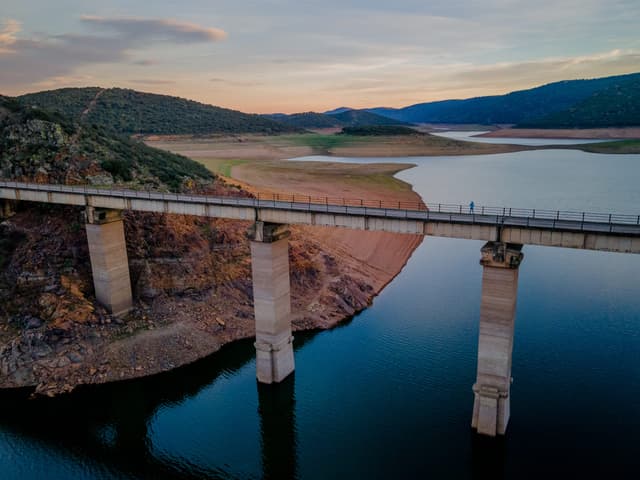 Ground-level photograph of Cíjara reservoir on the Guadiana with calm water reflecting oak woodland.