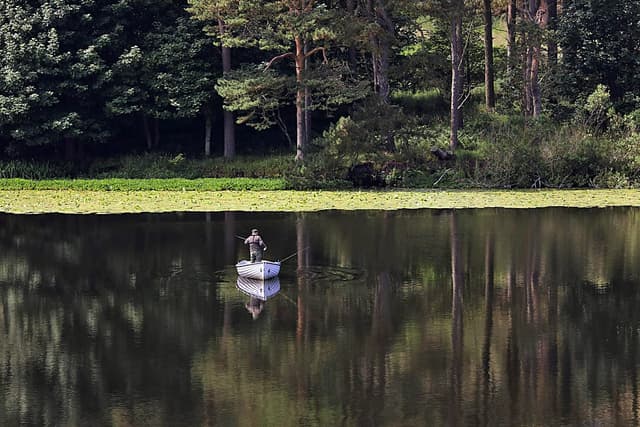 An angler fishing from a boat on the open water of Coldingham Loch, Scottish Borders.