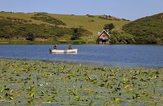 Angler fishing at Coldingham Loch with the lochside cottage and boathouse in the background.