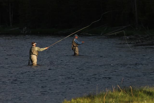 Two anglers casting fly rods while wading the Firehole River at golden hour, Yellowstone National Park.