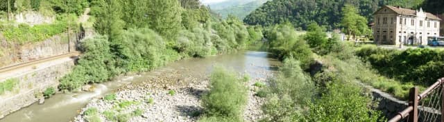 The Río Aller, a gravel-bedded river lined with trees, flowing through a green valley near Bustiello, Asturias, Spain.