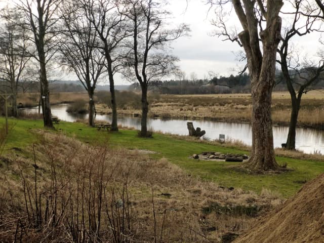 The Gudenå river winding through a grassy meadow near Resenbro, Denmark, lined with bare trees