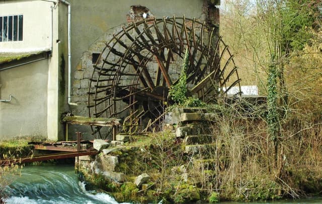 A historic stone watermill with a large wooden waterwheel, with the Durdent River flowing past in the foreground.
