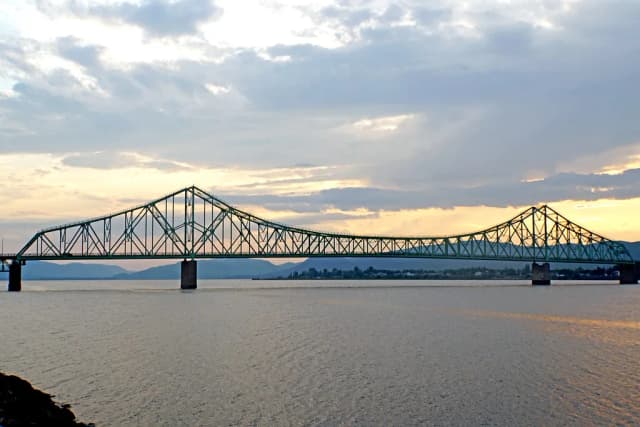 A large steel truss bridge spanning the wide Restigouche River at sunset, with mountains in the background.